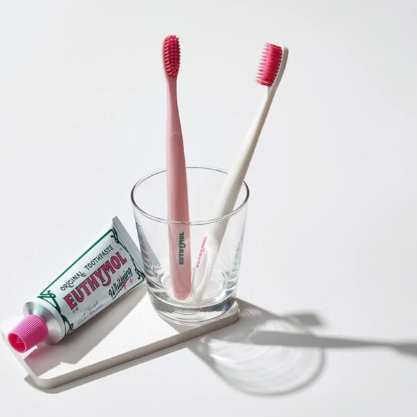 Euthymol Whitening Zahnbürste – Weisse Handzahnbürste mit Flex-Firm-Technologie für sanfte Plaque-Entfernung. Abbildung Zahnbürsten im Glas mit Zahnpasta.