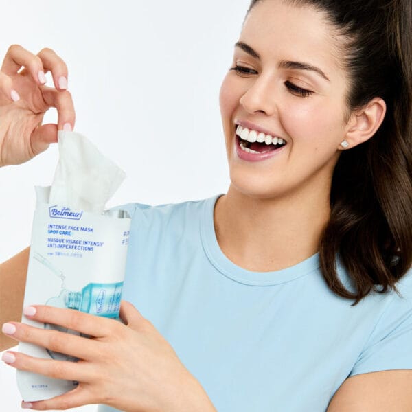 Dr. Belmeur Spot Care Intense Face Mask 30ml - masque en tissu apaisant à l'huile d'arbre à thé, à l'acide salicylique et au panthénol pour les peaux impures. Figure Femme sortant le masque de son emballage. 