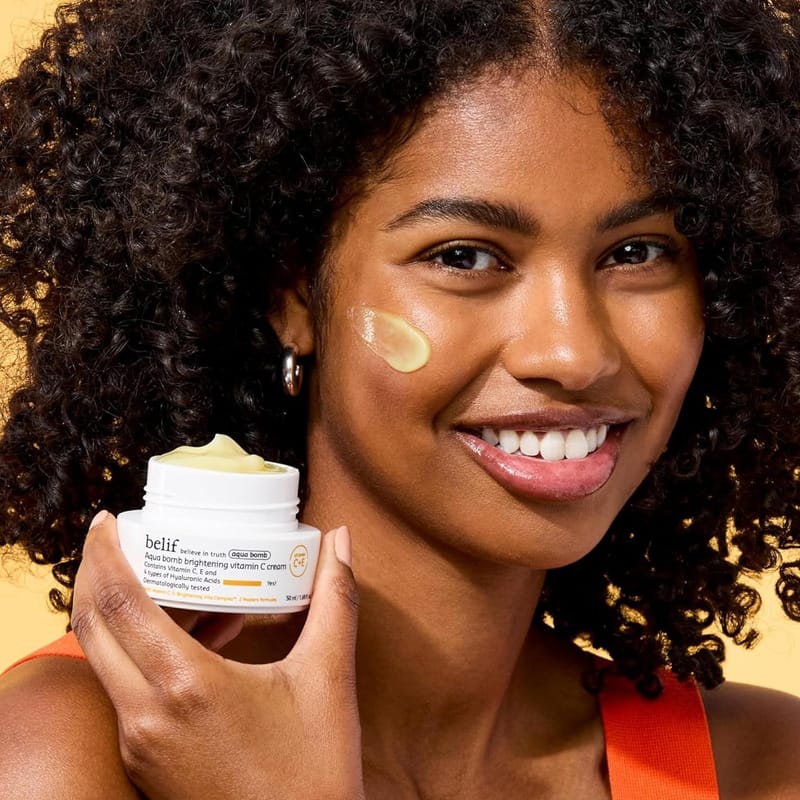 belif Gel-crème vitaminé ultra-léger à l'acide hyaluronique & aux antioxydants pour une peau éclatante et rebondie 50ml, Image Femme tenant le produit en l'air et ayant de la crème sur le visage